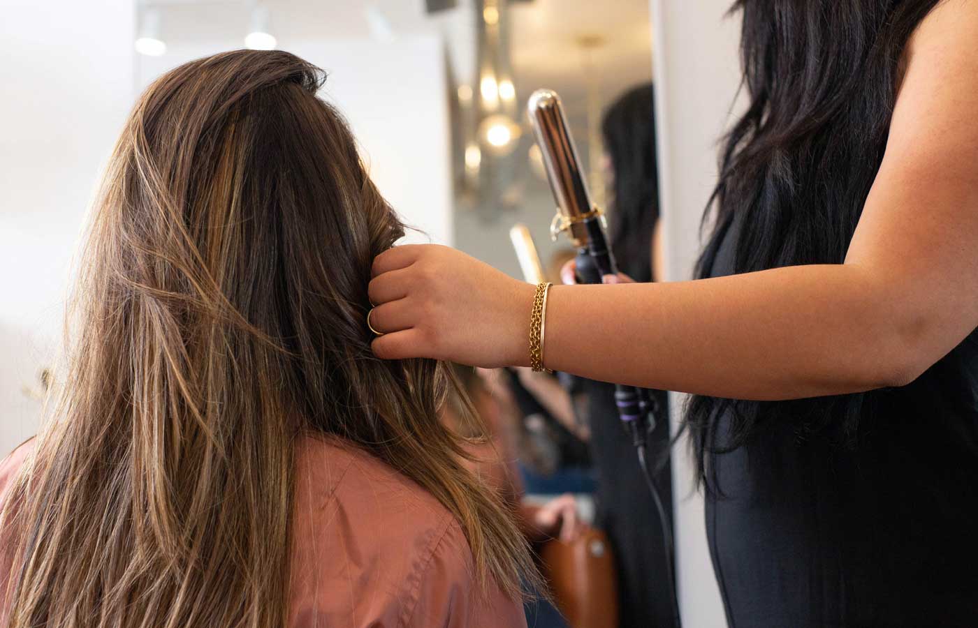 Shows a woman curling a client's hair with a heated styler