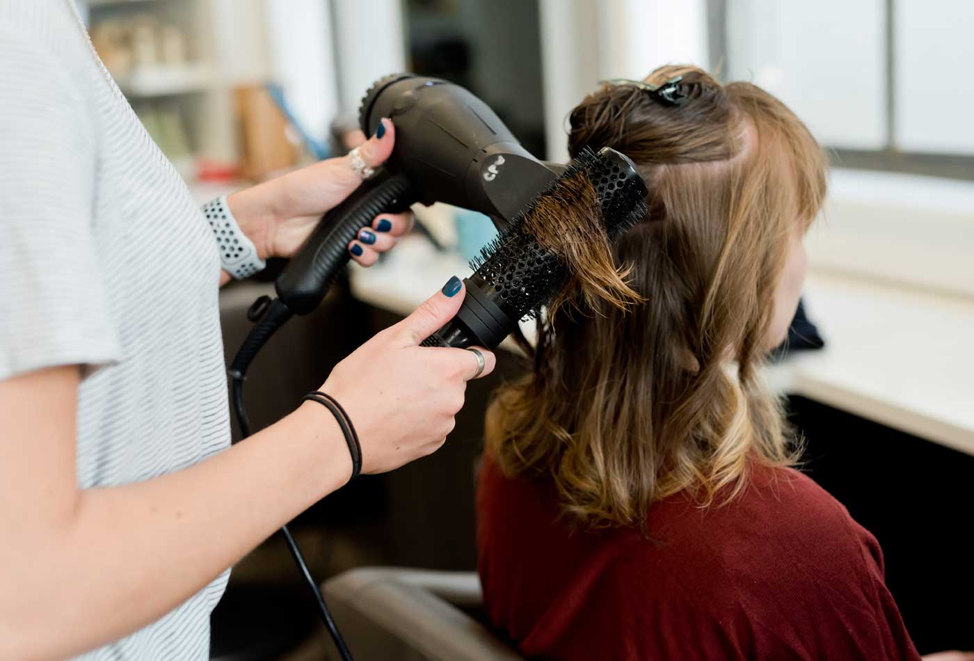 Shows a stylist blow-drying a customer's hair