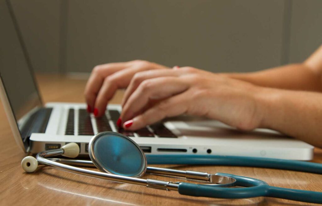 shows an image of someone typing on a laptop next to a stethoscope - Professional Medical Malpractice Insurance
