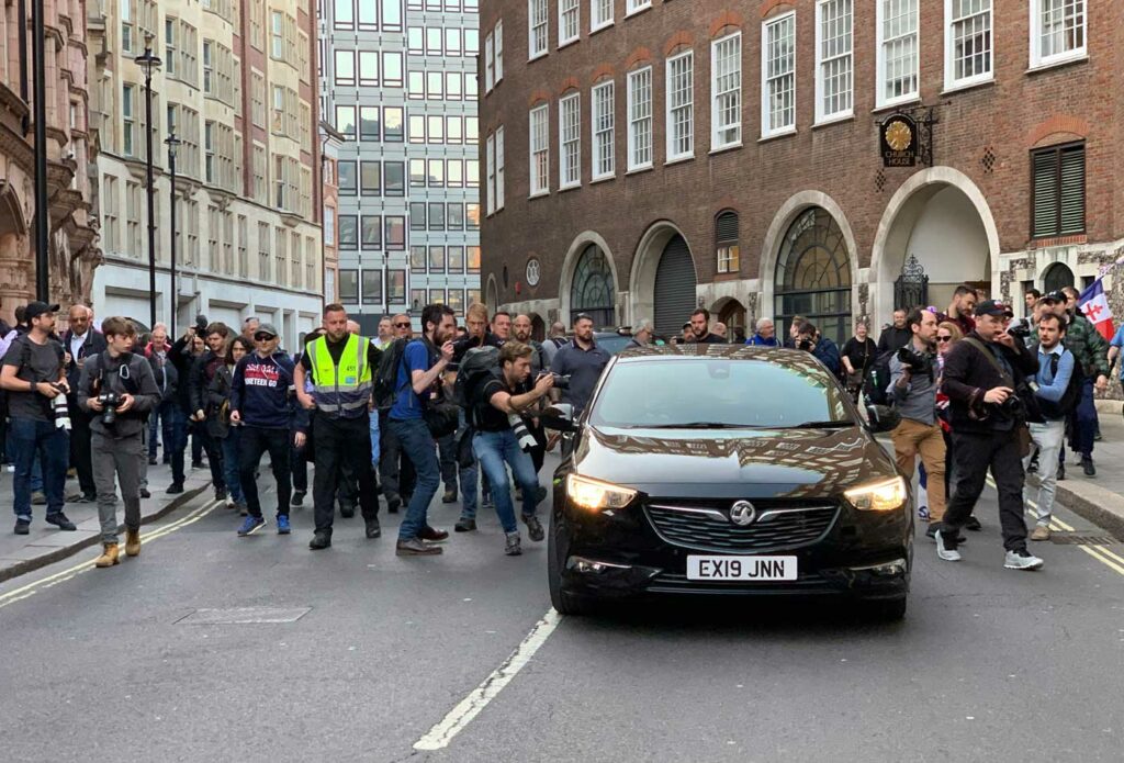 shows a crowd of a people next to a black car - security insurance